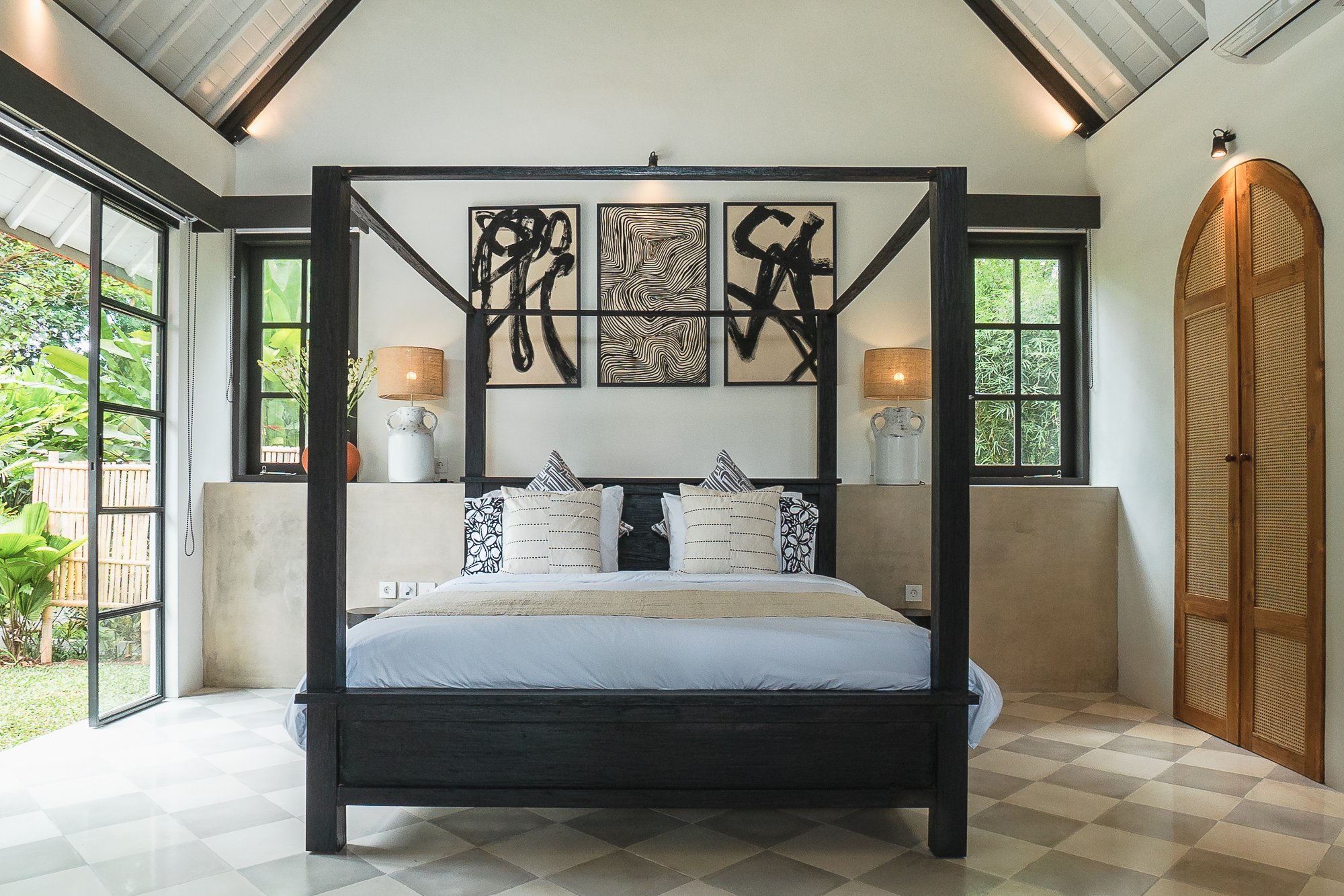 Bedroom with black four-poster bed, abstract wall art, and open doors to a garden.