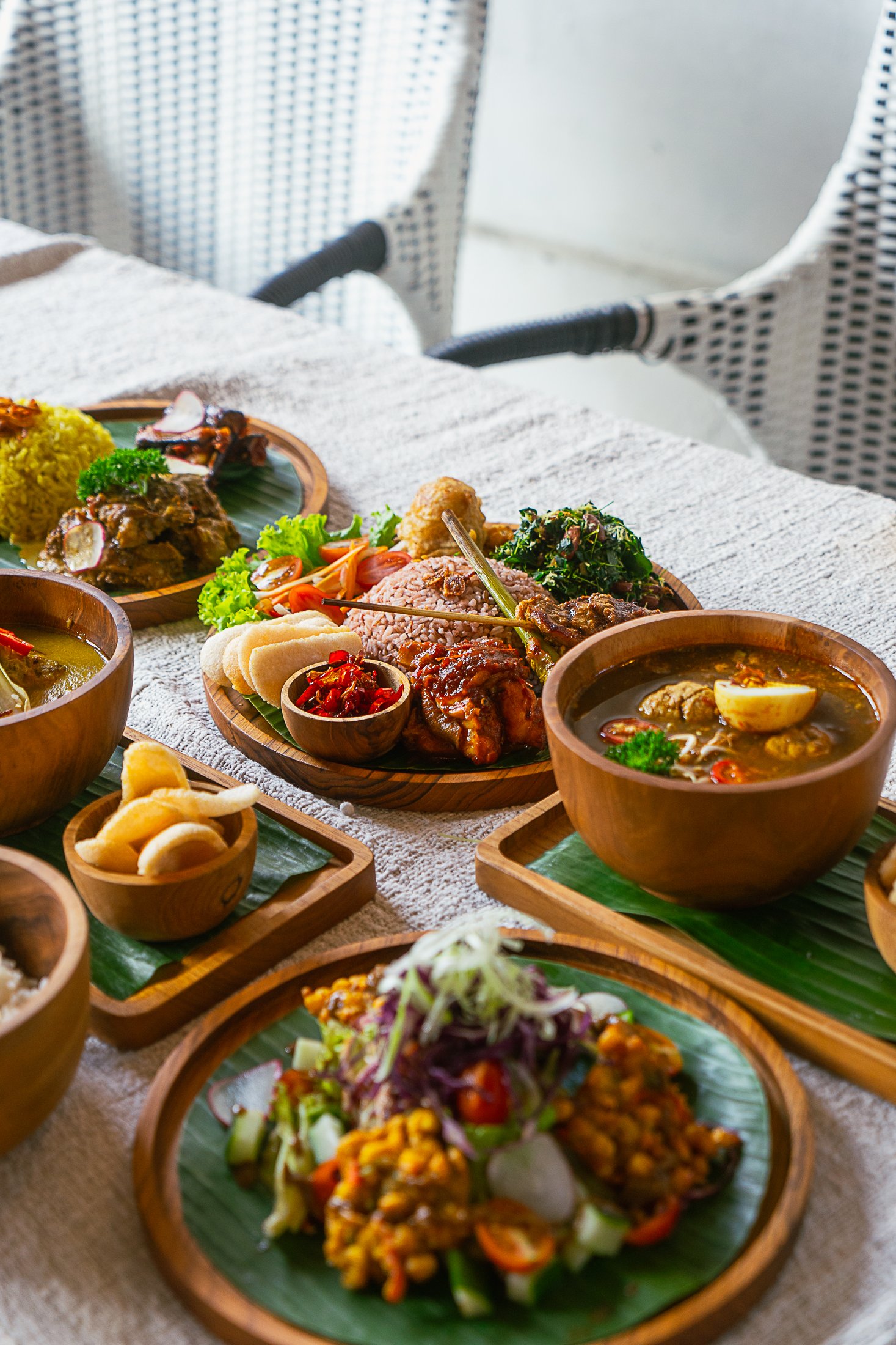 A table with various traditional Asian dishes served on wooden and ceramic plates and bowls, including curry, rice, salad, and soup.